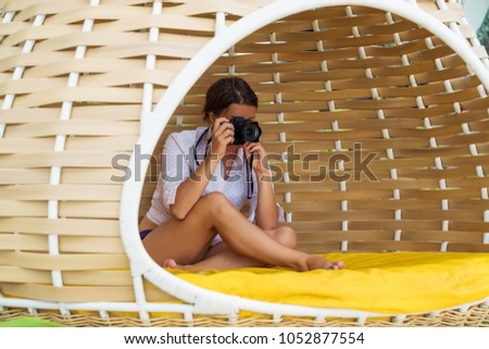 Caucasian woman sitting in egg lounger and making photo with camera like a spy. Hobby during vacation