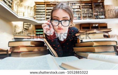 Smart blonde girl wears glasses studying at the library table full of books