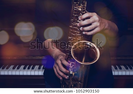 musician plays alto saxophone over piano with Bokeh light  background
