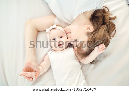 Top view of a happy mother kissing a baby lying on a bed.