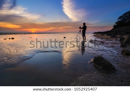 Silhouette of a passionate photographer capturing the amazing sunset colours at the beach with a low tide