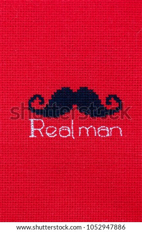 Black mustache embroidered on red fabric. The inscription "Real Man".