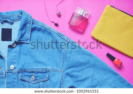 Flat lay fashion background. Blue denim jacket, headphones, perfume bottle, red nail polish and yellow clutch on a pink. Summer feminine items top view photo