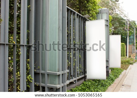 Vertical banners are hanging on metal line fence which covered with greenery plant. 