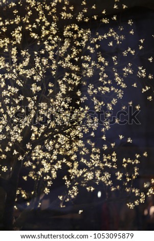 Close up indoor view of an artificial tree illuminated with many small lamps. Pattern of lighted points located on branches with a dark background. Decorative elements in the night. Abstract image. 