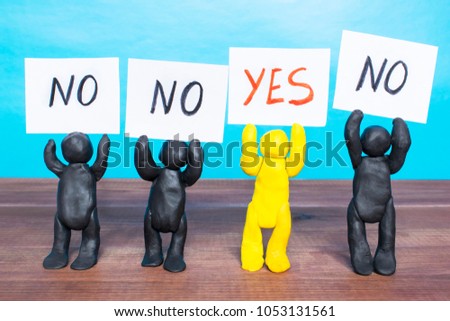 Plasticine people holding notes with words Yes and No on the wooden table. 