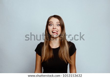 Positive emotions and feelings on white background.Caucasian female with long hair, wearing black T-shirt, fooling around in front of the camera, making funny faces.put out the tongue