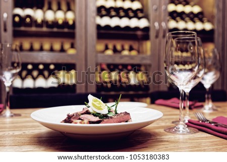 Roast beef appetizer on table, wine racks in blurred background, toned picture