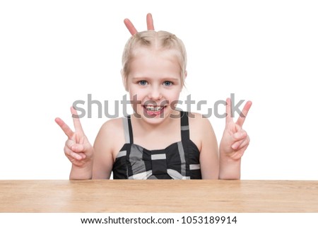 Girl sitting at table making horns with hands isolated on white background