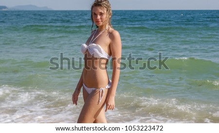 Pretty young girl dressed up in white swimwear on the beach near water