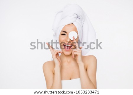 Removing makeup. Beauty and spa. A beautiful smiling woman with a towel on her head moisturizes or cleanses her face from makeup using cotton pads. Cosmetology. Women Health Royalty-Free Stock Photo #1053233471