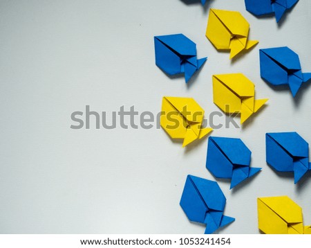 group of blue and yellow origami fish on white background with copy space. working in team concept. 