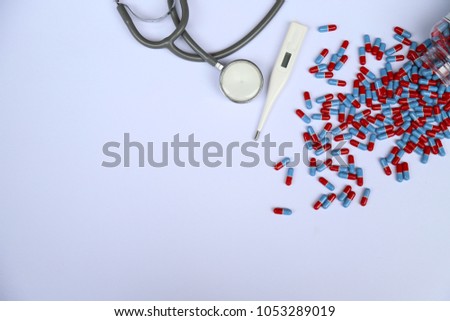 Closeup of drug capsules from the bottle with thermometer and stethoscope on white background. Shows the symbol of essential and professional medical and pharmaceutical services for good health.