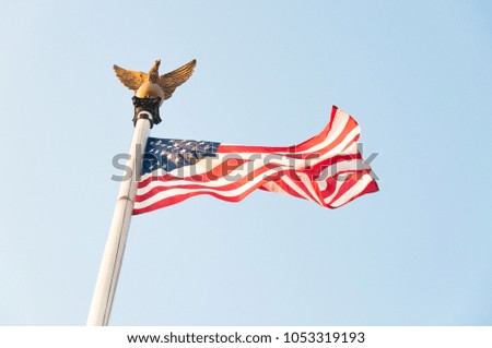 Stars and Stripes flag waving in the wind with blue sky and golden eagle.