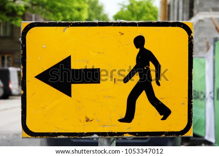 Traffic sign: on a yellow background a black silhouette of a walking man and a black arrow to the left against a city landscape background. Signs, symbols.