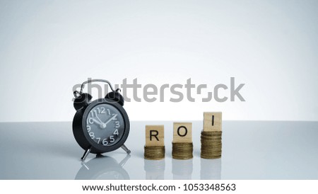 Return on Investment (ROI) Conceptual image with Black retro alarm clock with coins and wooden text block