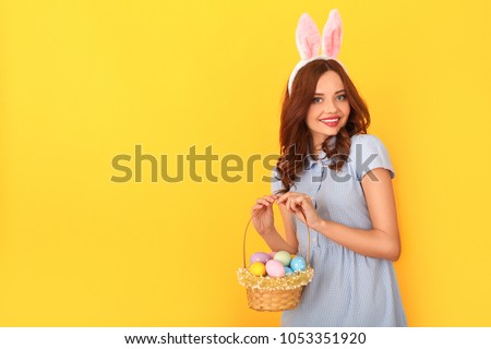 Young woman studio isolated on yellow wearing bunny ears holding basket with eggs joyful