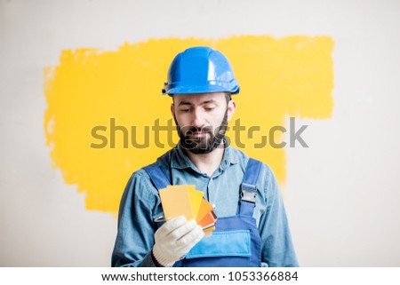Painter in blue workwear holding color swatches on the yellow wall background indoors