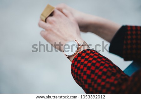 outfit details, chic woman wearing a stylish red pepita pattern jacket and a rose gold watch. detail shot of a watch and ring on a womans hand