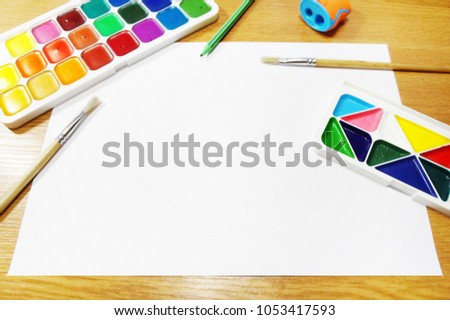 Art concept. Watercolor paints, brushes, pencil, sharpener and white paper on wooden table. Set of artist tools and colorful stationery for banner or card, blank sheet, empty space for text or sign