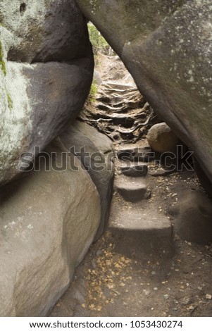 the picture depicts an uncommon staircase made of rocks that is found under a big boulder