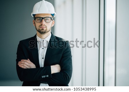 Successful engineer or architect, Joyous businessman with crossed arms wearing helmet on office background