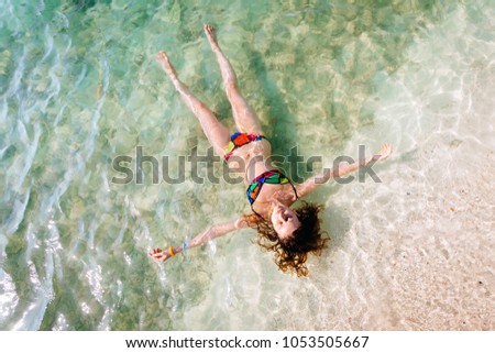 Top view of young woman in a bright bikini is swimming in the transparent, blue sea. Aerial view of slim woman lying and floating on the water of Andaman sea. Phuket, Thailand.