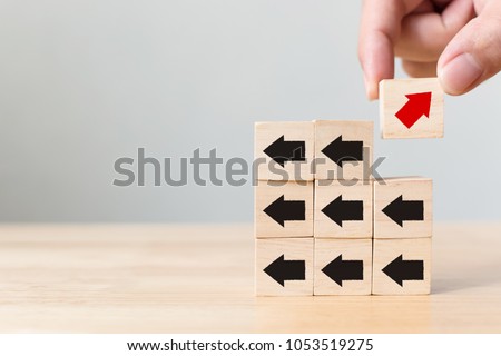 Hand picked wooden block with red arrow facing the opposite direction black arrows, Unique, think different, individual and standing out from the crowd concept Royalty-Free Stock Photo #1053519275