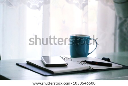 Home working desk near window in the morning with open diary, coffee cup, smartphone, document closeup blur background