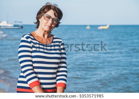 Pretty elderly woman in sunglasses on vacation by sea on background of ship
