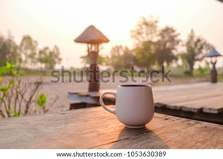 a selective focus picture of a cup of coffee on wooden table at farm in the morning sunrise