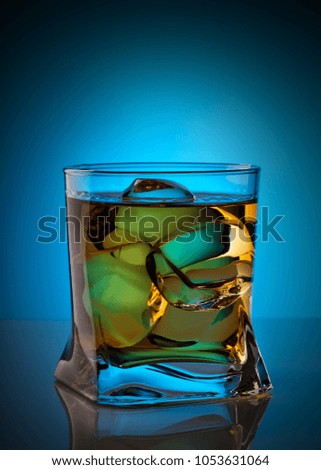 Whiskey with ice cubes in transparent glass on blue background