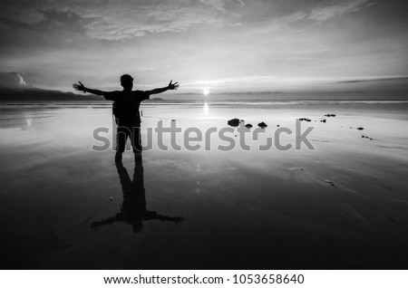 Self portrait of a man standing and having his hands up while looking at the beautiful sunset (black and white)