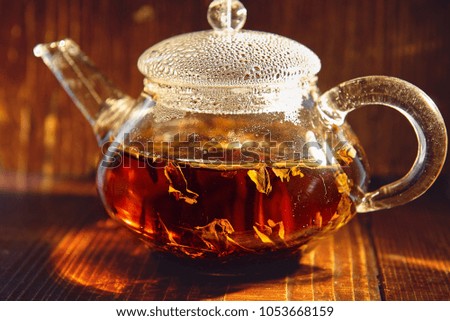 Transparent glass teapot with black tea on a brown background 