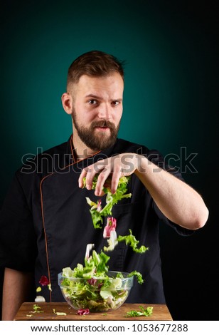 Portrait of a handsome male chef cook making tasty salad on a blurred aquamarine background