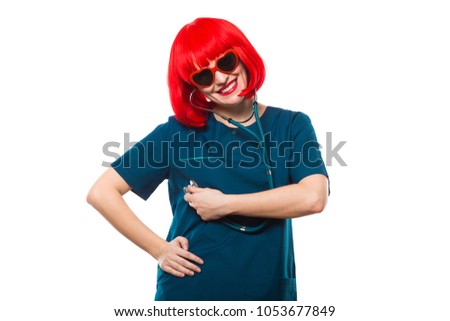 Attractive funny smilling caucasian brunette female doctor in red wig and red sunglasses standing in office fooling