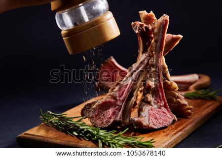 Rack of lamb with rosemary on wooden cutting board over dark background, side view, selective focus