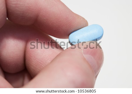Fingers hold a blue tablet. Close-up, shallow depth of field.