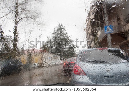 Blurry car silhouette seen through water drops on the car windshield. Rainy days, rain background