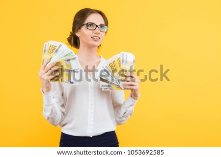 Portrait of confident beautiful happy young business woman with money in her hands standing on yellow background