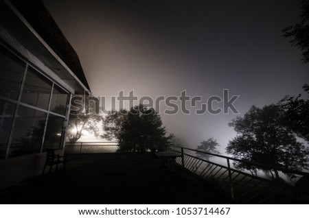 Mountain night landscape of building at forest in foggy night with moon. Green meadow, big trees and abandoned house at night