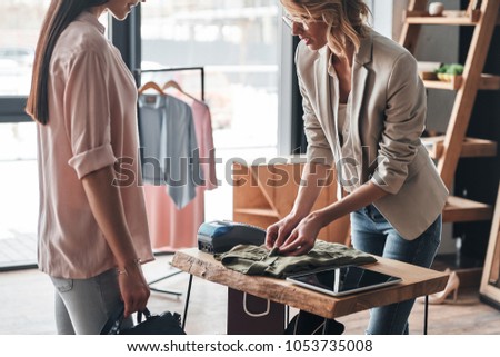 Just one moment. Beautiful young woman folding a shirt for her customer while working in the fashion boutique                 Royalty-Free Stock Photo #1053735008