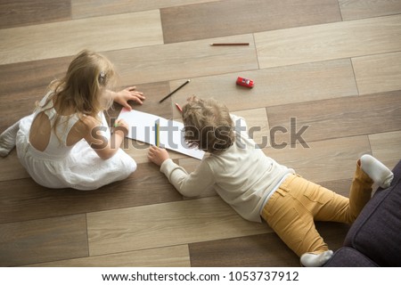 Kids sister and brother playing drawing together on wooden warm floor in living room, creative children boy and girl having fun at home, siblings friendship, underfloor heating concept, top view Royalty-Free Stock Photo #1053737912
