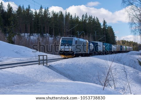 Freight train in winter landscape with forest and blue sky in background, picture from Northern Sweden.