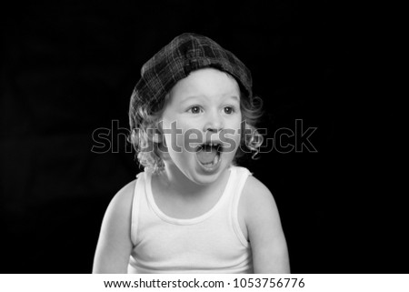 A black and white portrait of a little boy wearing a white tank top who looks surprised, excited and shocked. There is room for text and room for words on a solid black background.