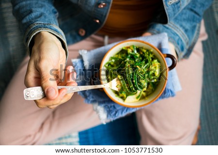 Young woman holds in hands healthy seaweed chuka salad with greens, turnip, rocket salad, spinach, radish, dill, onion sprouts, oil. With legs and carpet. Top view. Raw, vegan, vegetarian food Royalty-Free Stock Photo #1053771530
