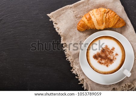 Cup of cappuccino coffee and croissant on dark table, top view Royalty-Free Stock Photo #1053789059