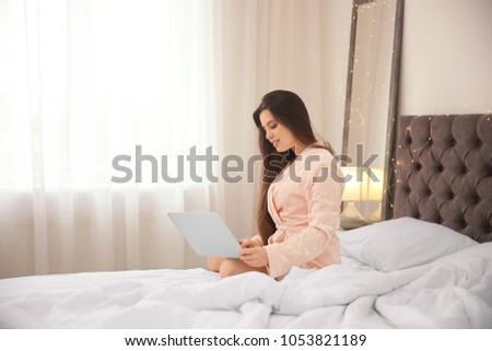 Young woman using laptop on bed in hotel room