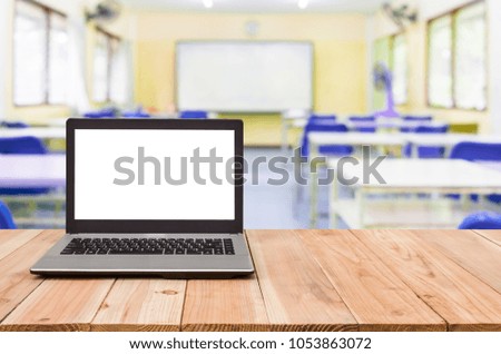 Computer on the table, blur image of inside the classroom as background.