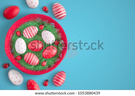Easter eggs in red basket with ladybug decorations. Top view of blue surface with free space for text.